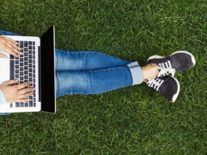Partial view of a person sitting on grass typing on a laptop